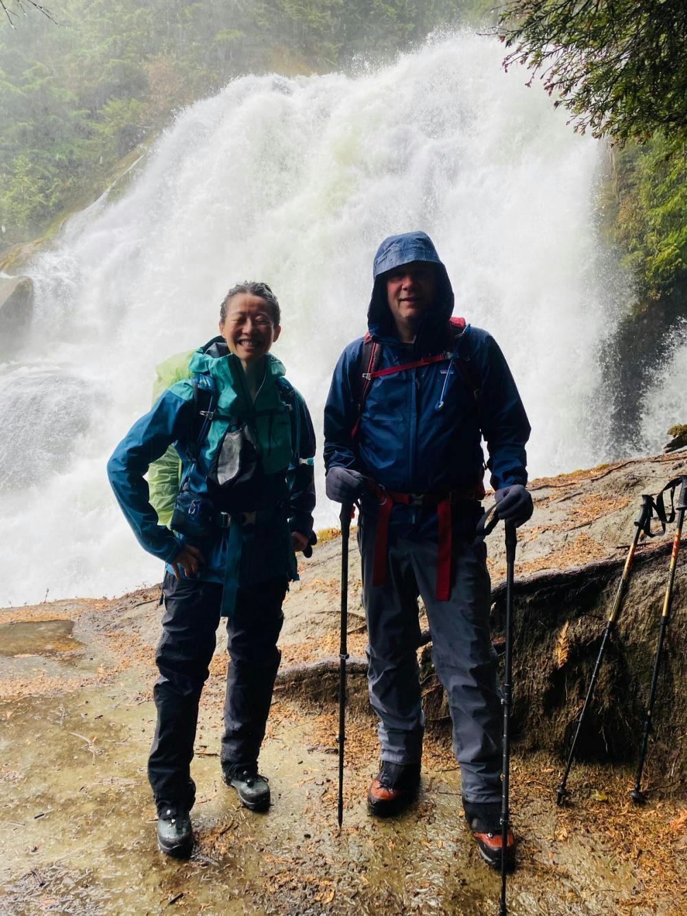 Doug and his wife smiling on a hike in front of a waterfall