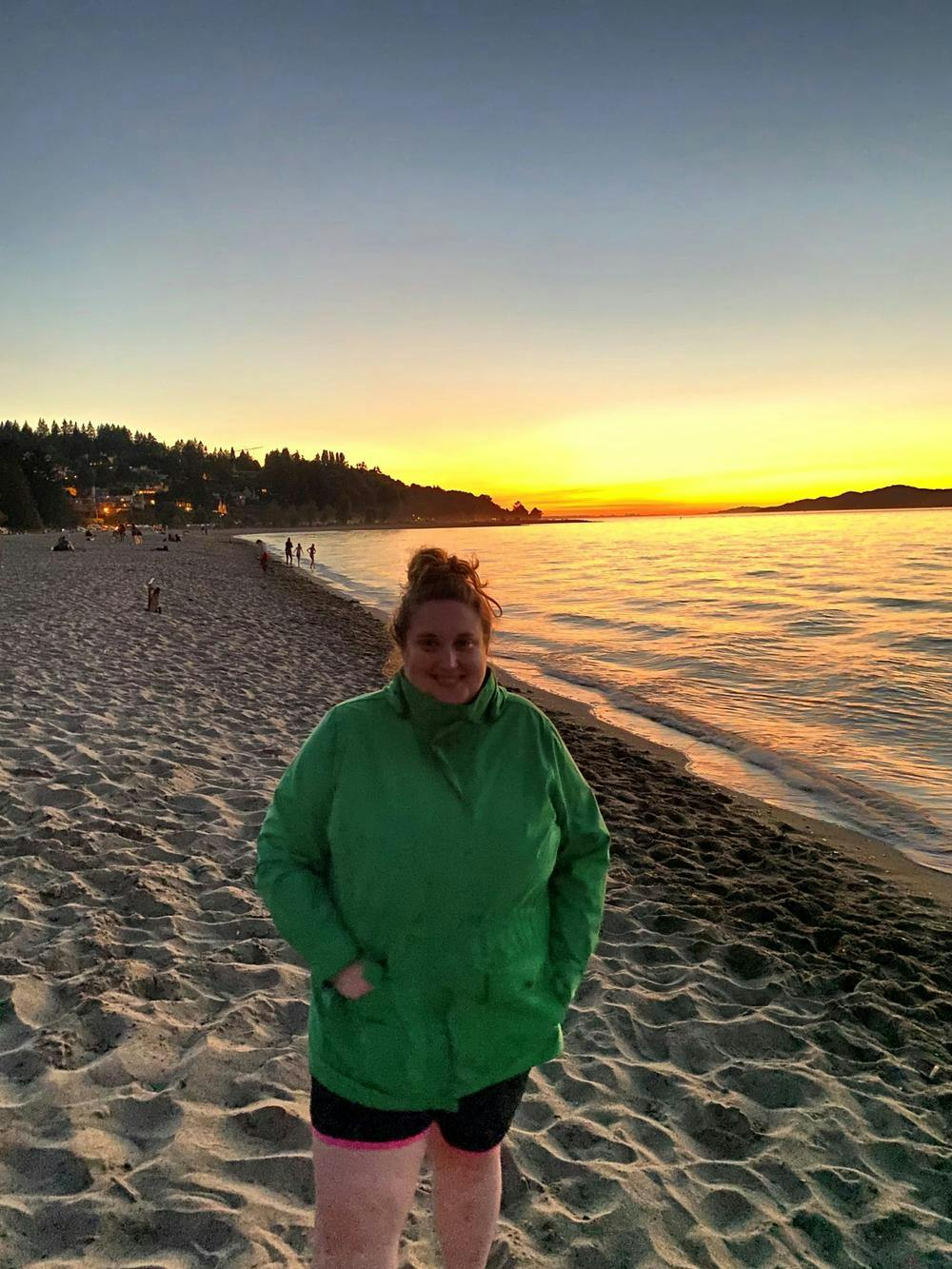 Katie standing on a beach in front of a sunset over the water