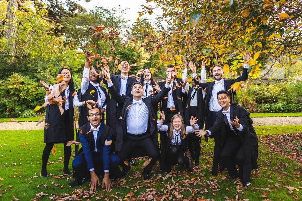 Liam and a group of classmates in suits and throwing fall leaves in the air with big smiles