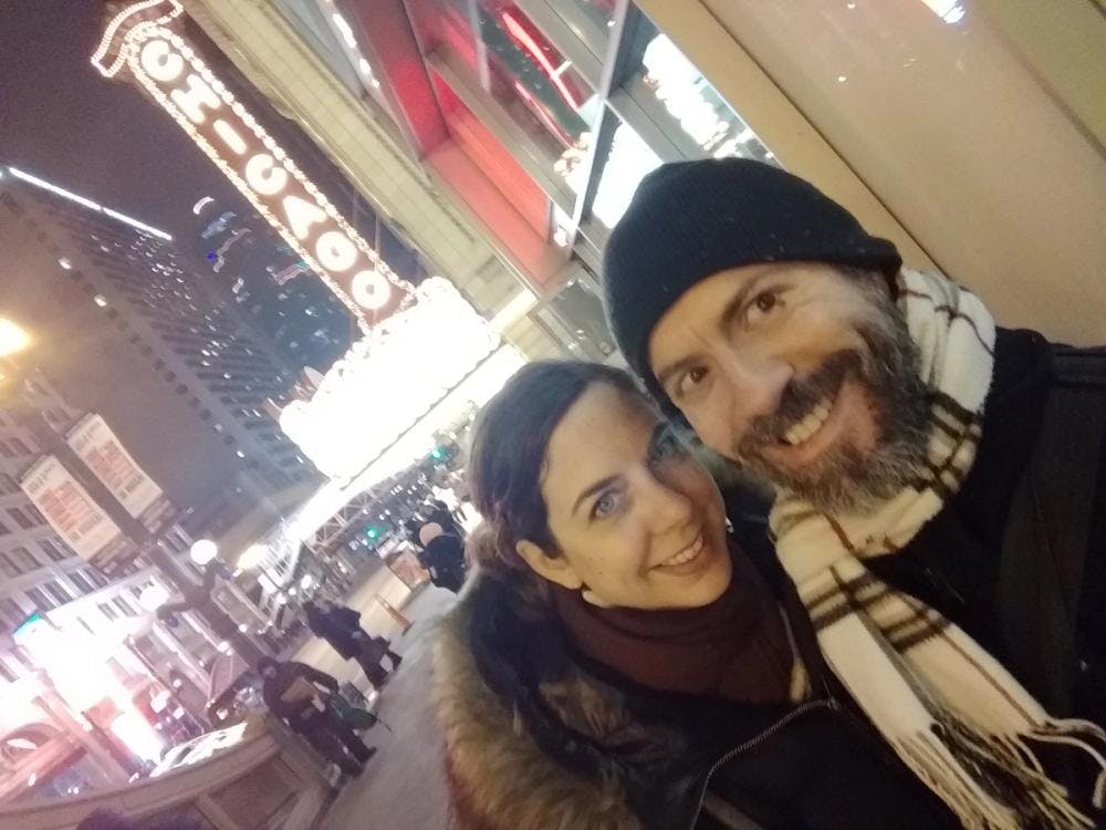 Selfie of Jennifer and her partner dressed in warm winter clothing and standing in front a neon Chicago sign