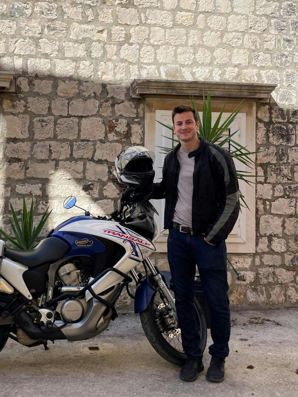 Kieran standing with a motorcycle in front of stone wall
