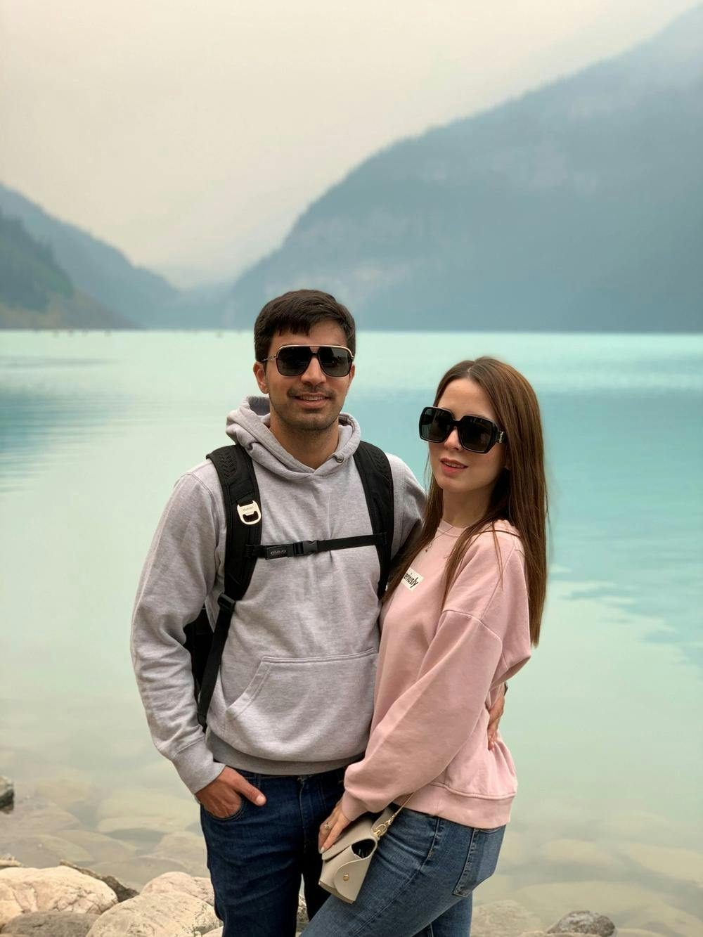 Baqar and his partner wearing sunglasses standing in front of a lake and mountains