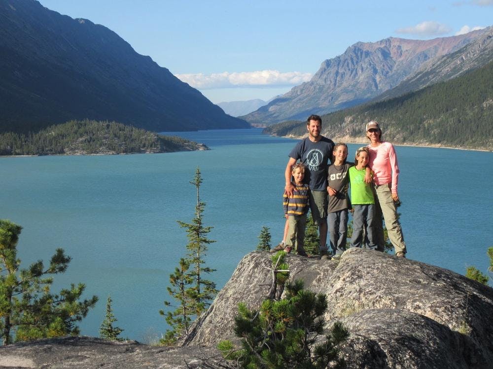 Alastair and his family standing on top of a large rock in front of a beautiful lake and mountains