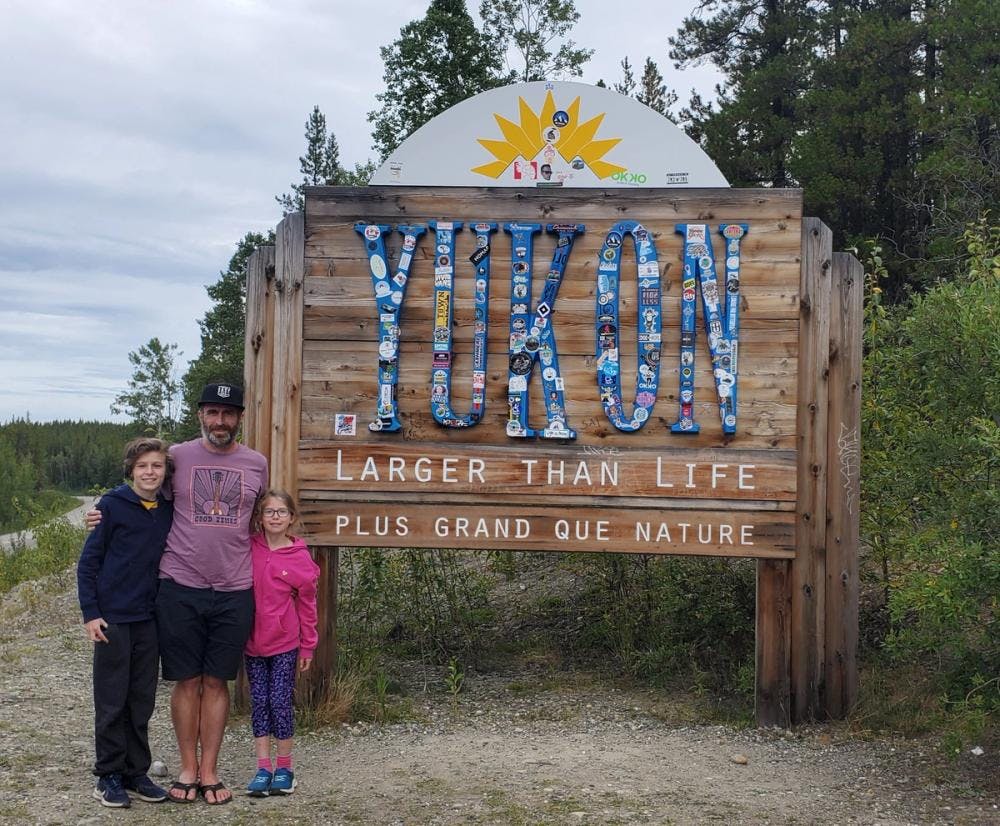 Earl with his two children in front of a sign welcoming them to the Yukon