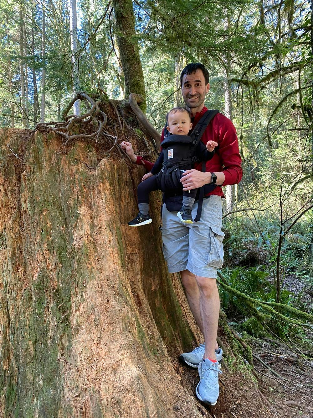 Rob and his child hiking in the woods standing next to a tree stump