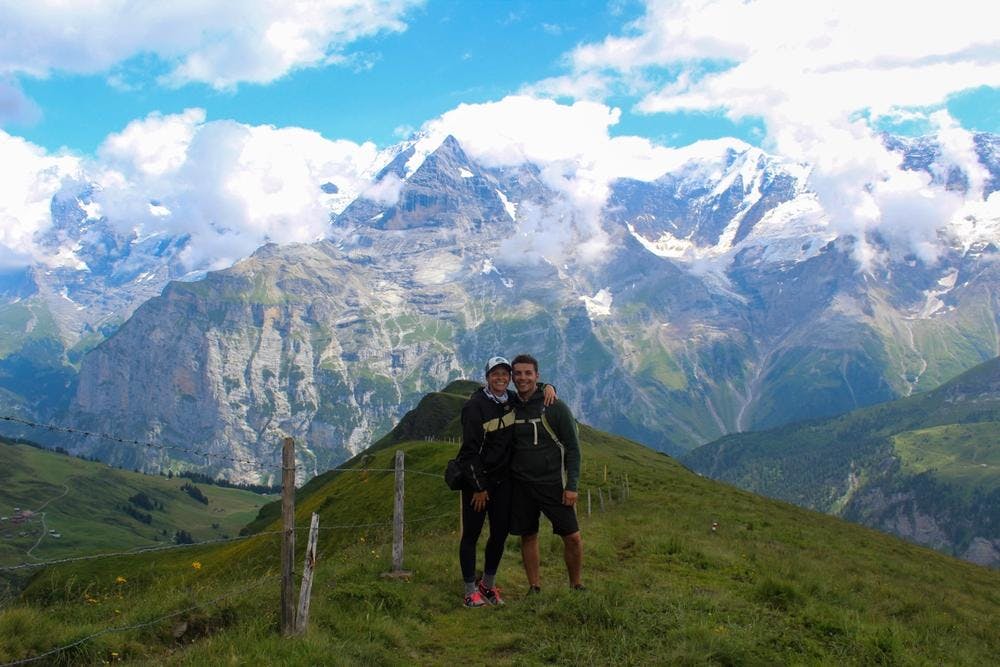 Liam Elbourne and his partner standing on a green mountain in front of other mountains