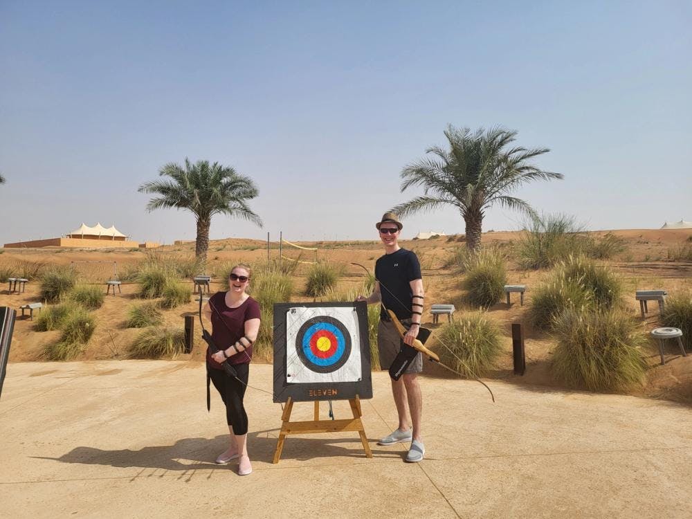 Couple standing next to a target practicing archery in an arid landscape