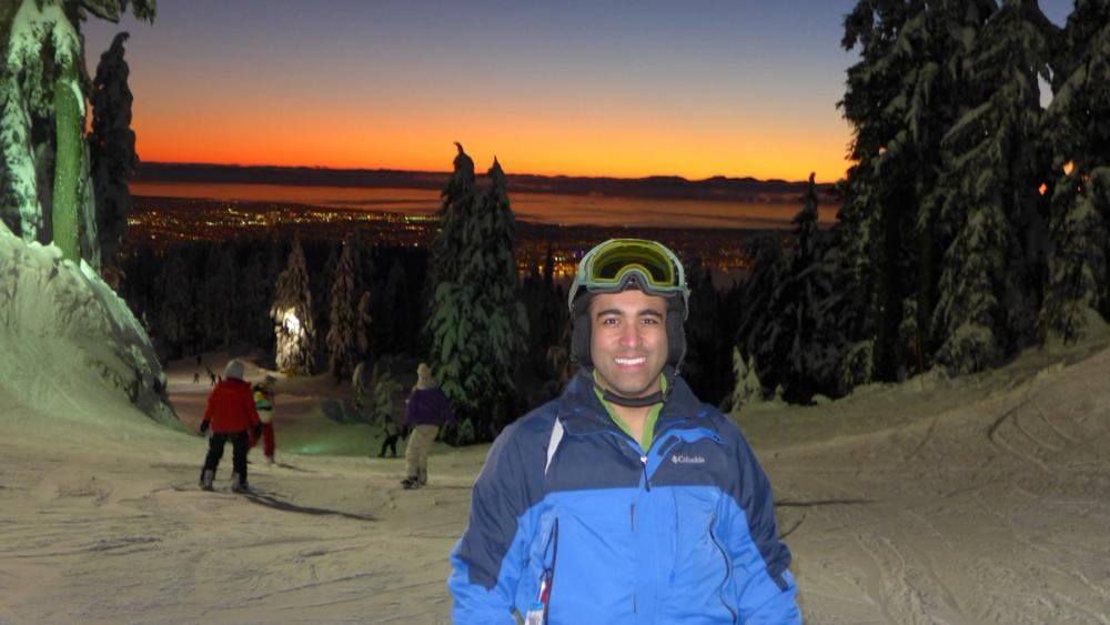 Ashwani smiling on a ski hill with Vancouver in the background