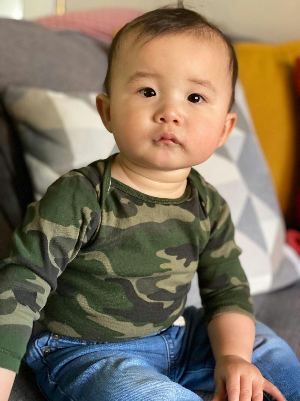 Rob's young child sitting up by himself in a green camo shirt and jeans