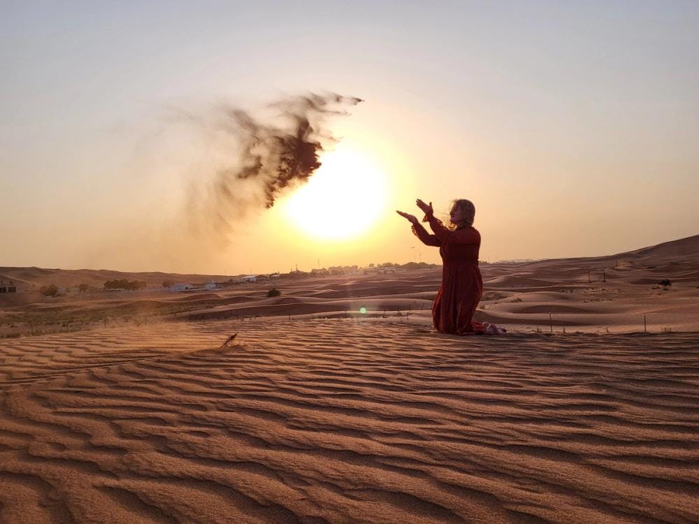 Girl in a red outfit throwing sand in the desert