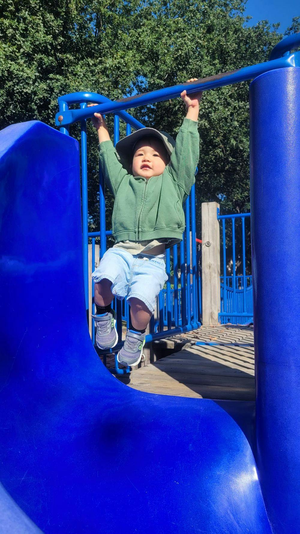 Rob's child hanging on a blue bar in a playground