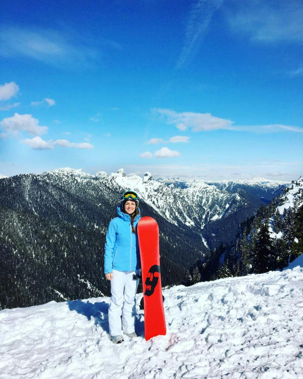 Alicia Stirling in blue and white snowboard gear holding a red snowboard on a snowy mountain